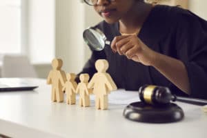 Judge with magnifying glass looking at little family figures standing